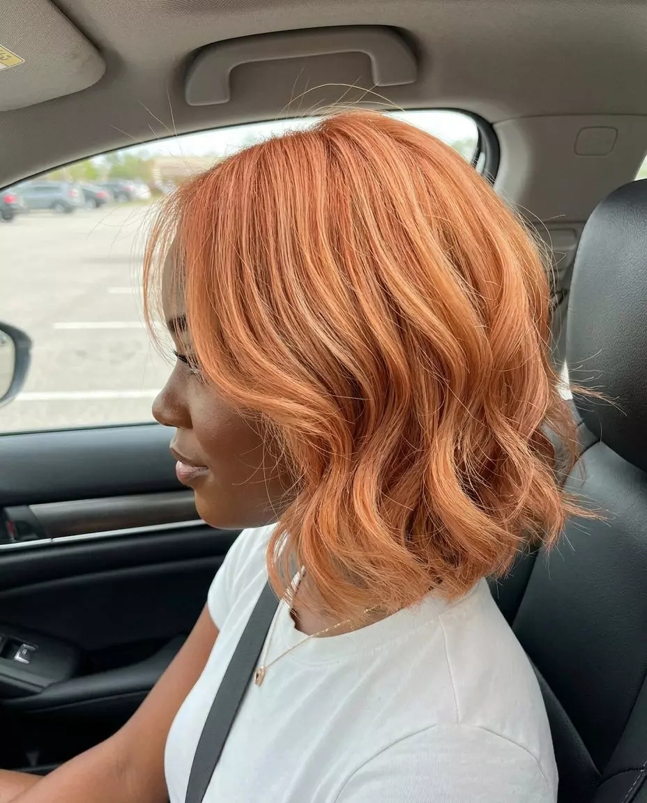 chin-length butterfly bob in apricot crush with strawberry blonde highlights, soft razored layers, no bangs for playful energy