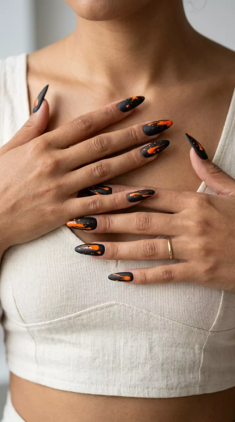 Sultry matte black nails with vivid orange abstract splatters. Neon summer nails 2026.