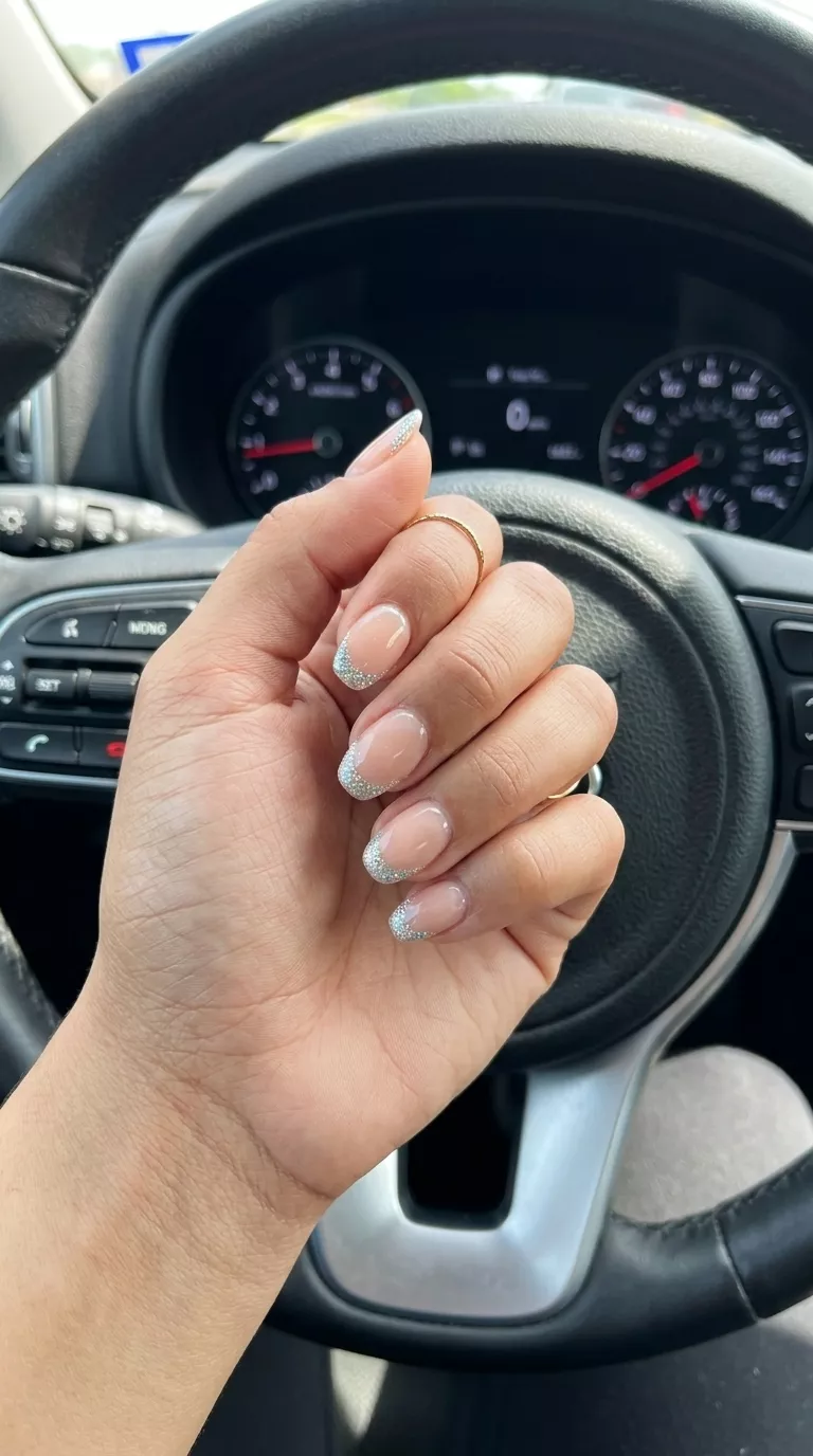 Chic short oval nails with sheer nude base and silver holographic glitter micro-French tip for summer glitter nails 2026.