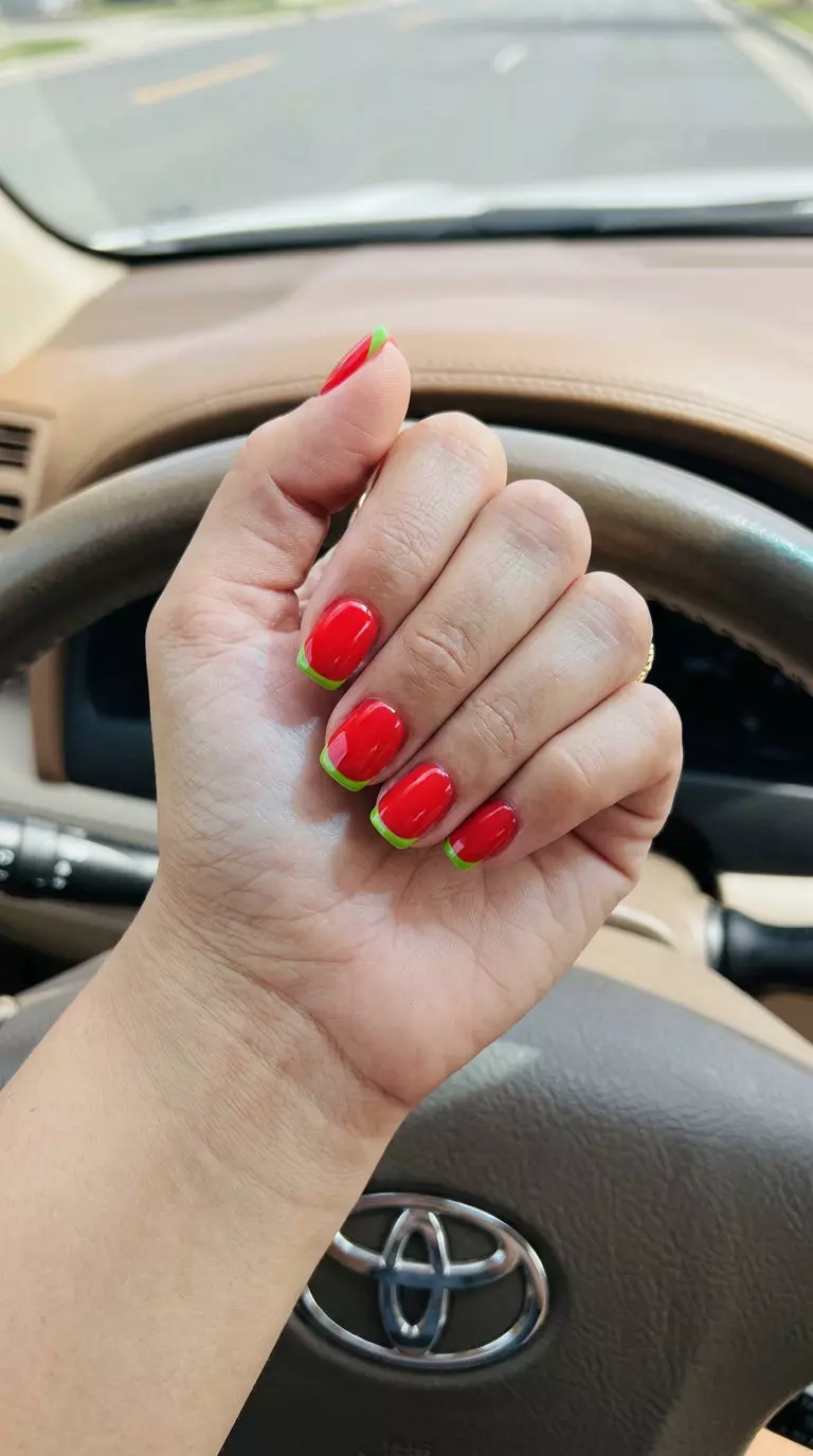 Glossy strawberry red and lime green French tip nails for summer strawberry nail ideas 2026. Playful chic picnic outfit.